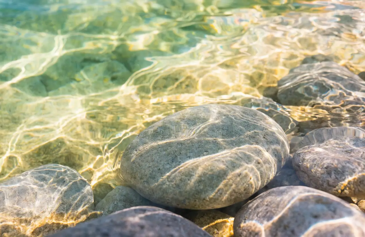 Smooth pebbles beneath clear water with rippling golden light